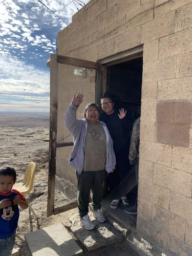 Hopi family waving from open door of cliff edge home.